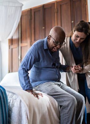 Home caregiver helping a senior man standing up at home